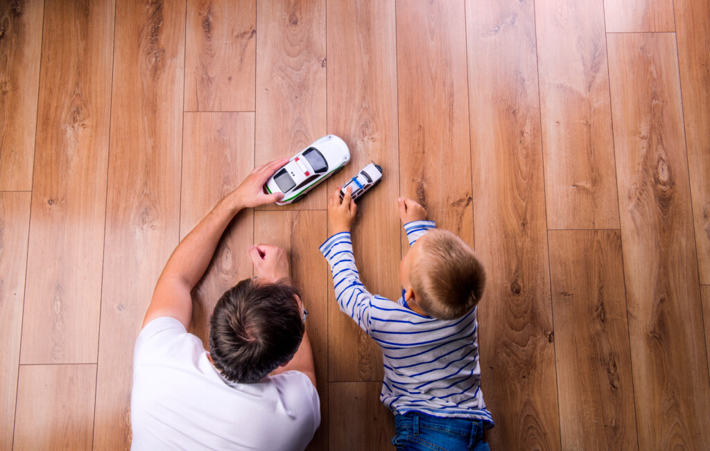 father and son playing with toy cars on hardwood floor